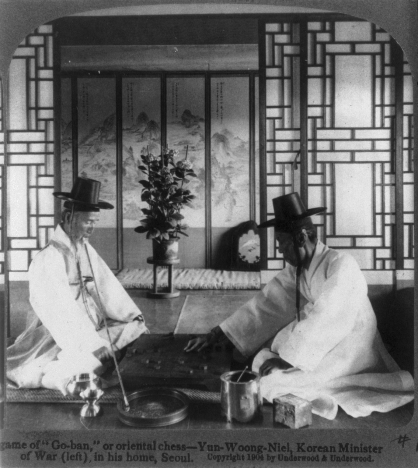 1904년 서울의 실내에서 두 사람이 판으로 보이는 물체를 사이에 두고 마주 앉은 사진